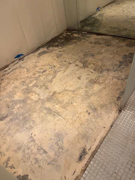 Commercial floor being prepped, with old adhesive scraped off the subfloor beside a mosaic tile section.