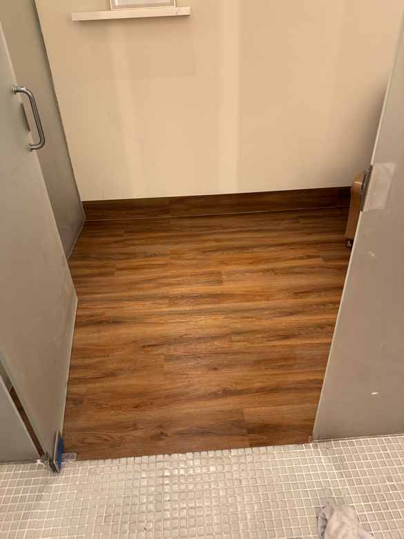Finished wood-look luxury vinyl plank seen through a doorway, with mosaic tile in the foreground.