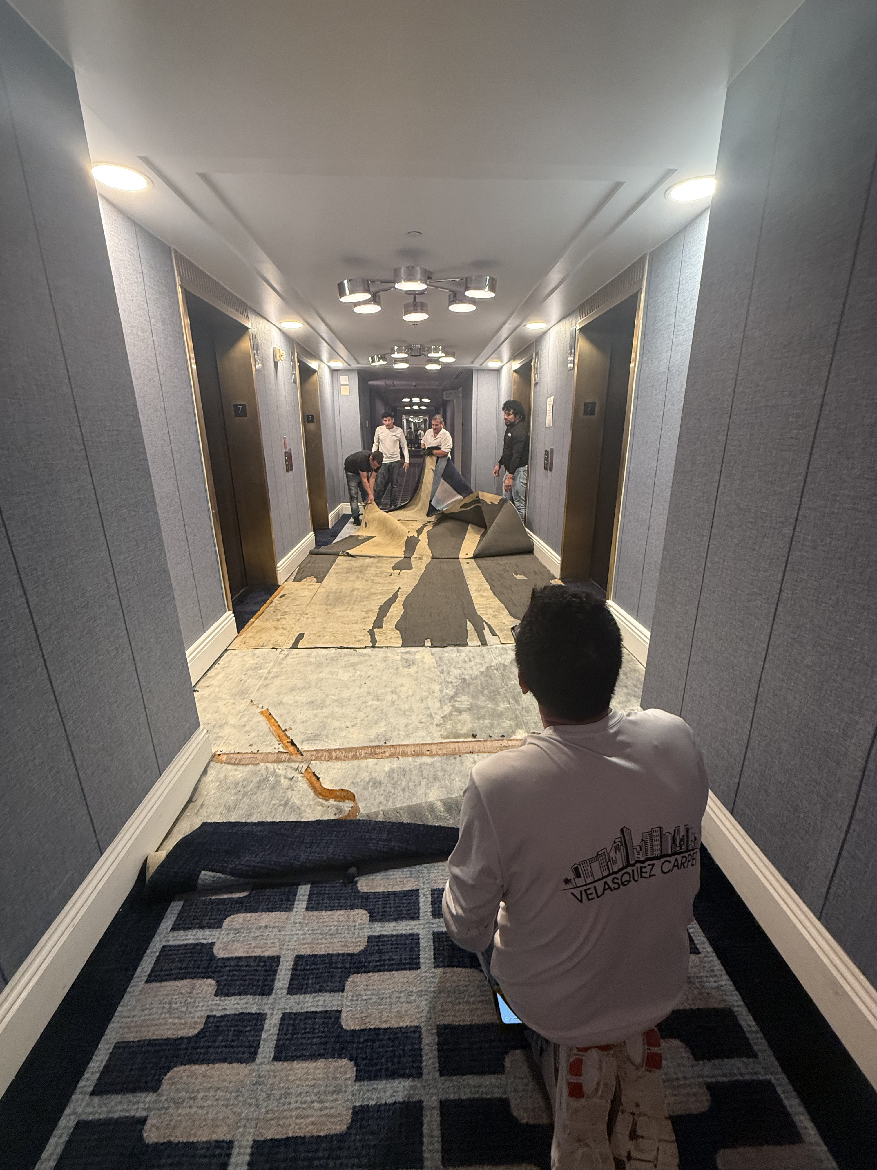 Glue-down hotel corridor carpet being lifted near the elevators