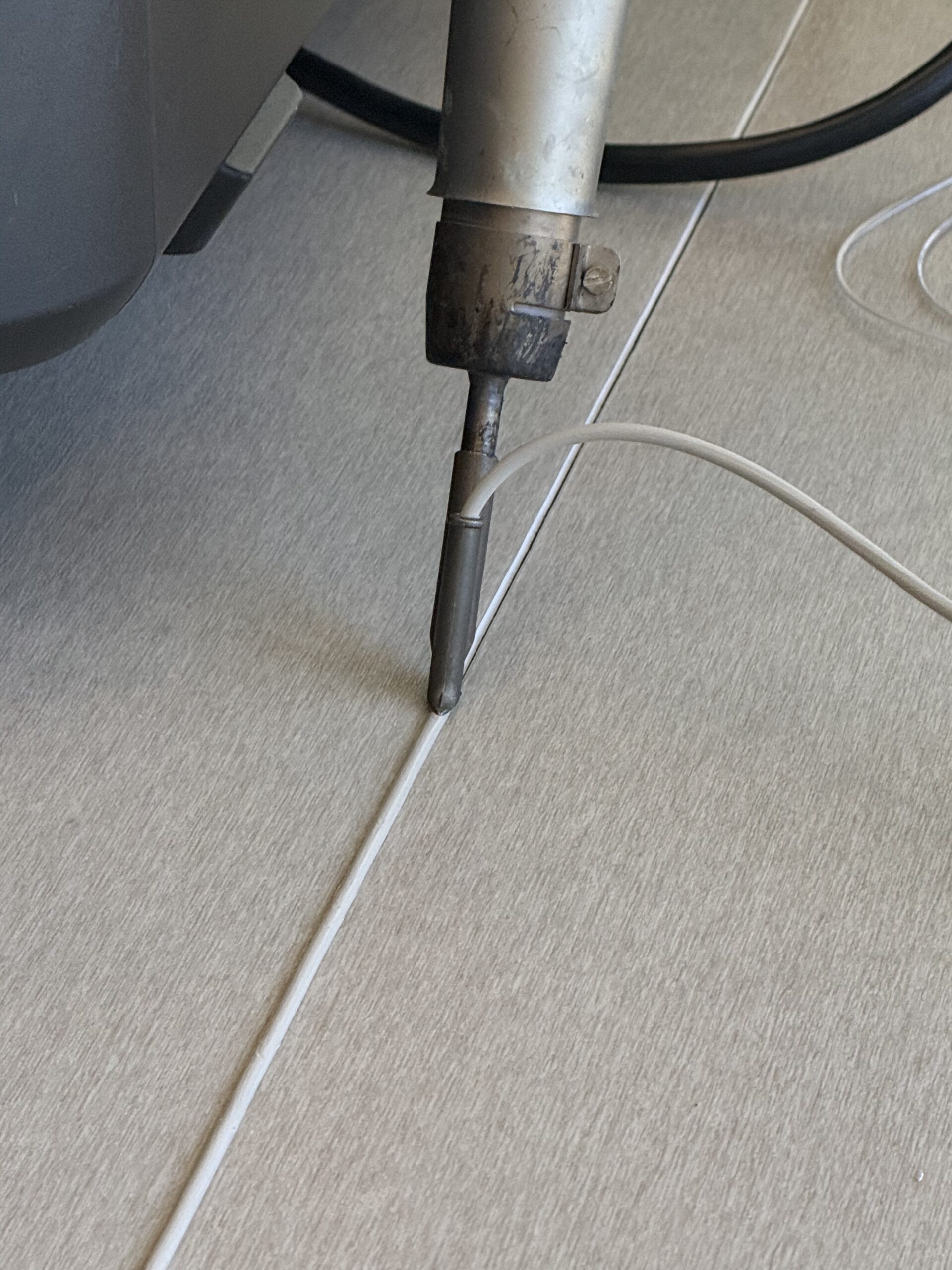 Hot-air welding gun feeding weld rod into a seam on commercial vinyl flooring