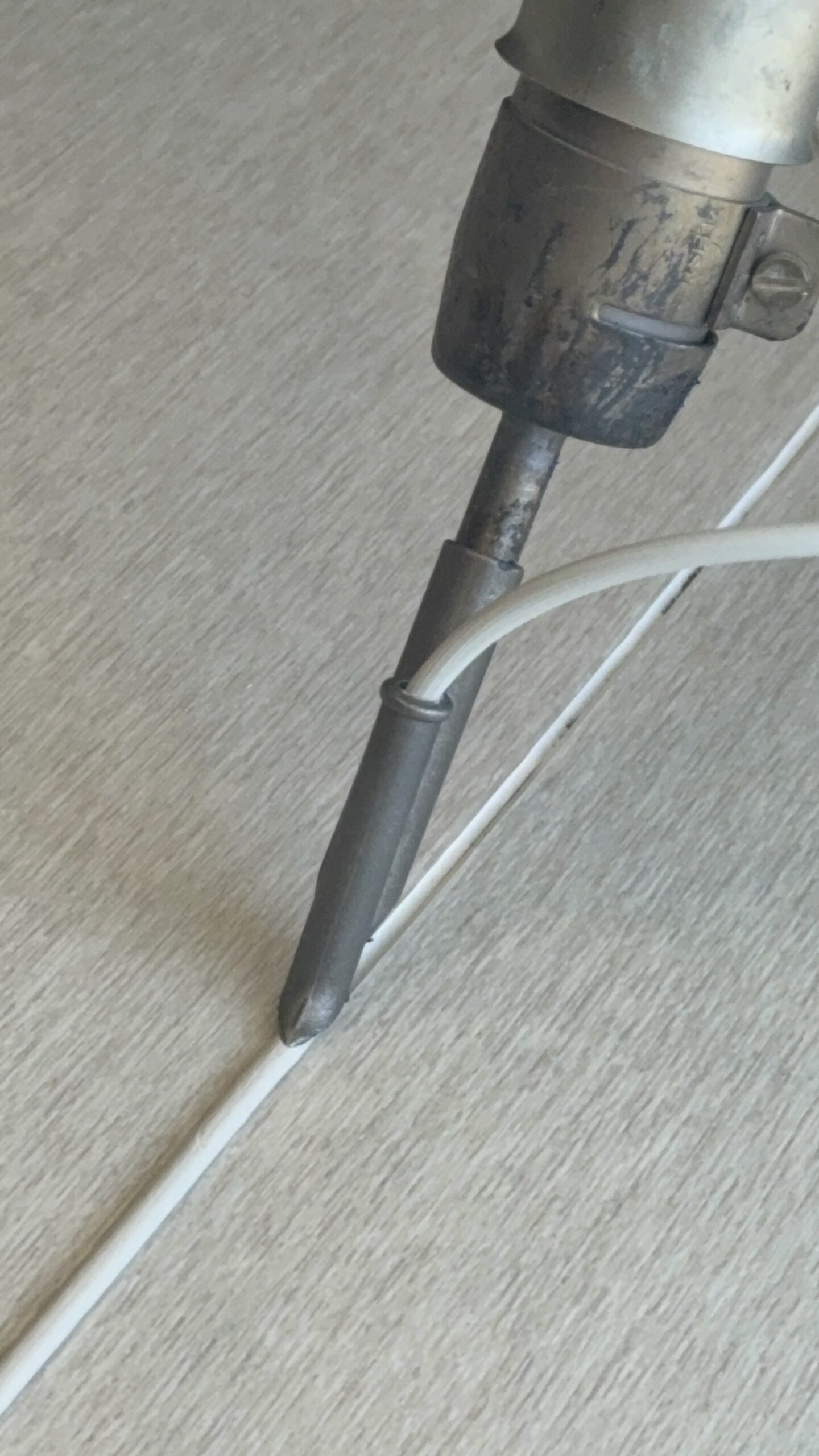 Close-up of a welding nozzle melting white weld rod into a vinyl floor seam