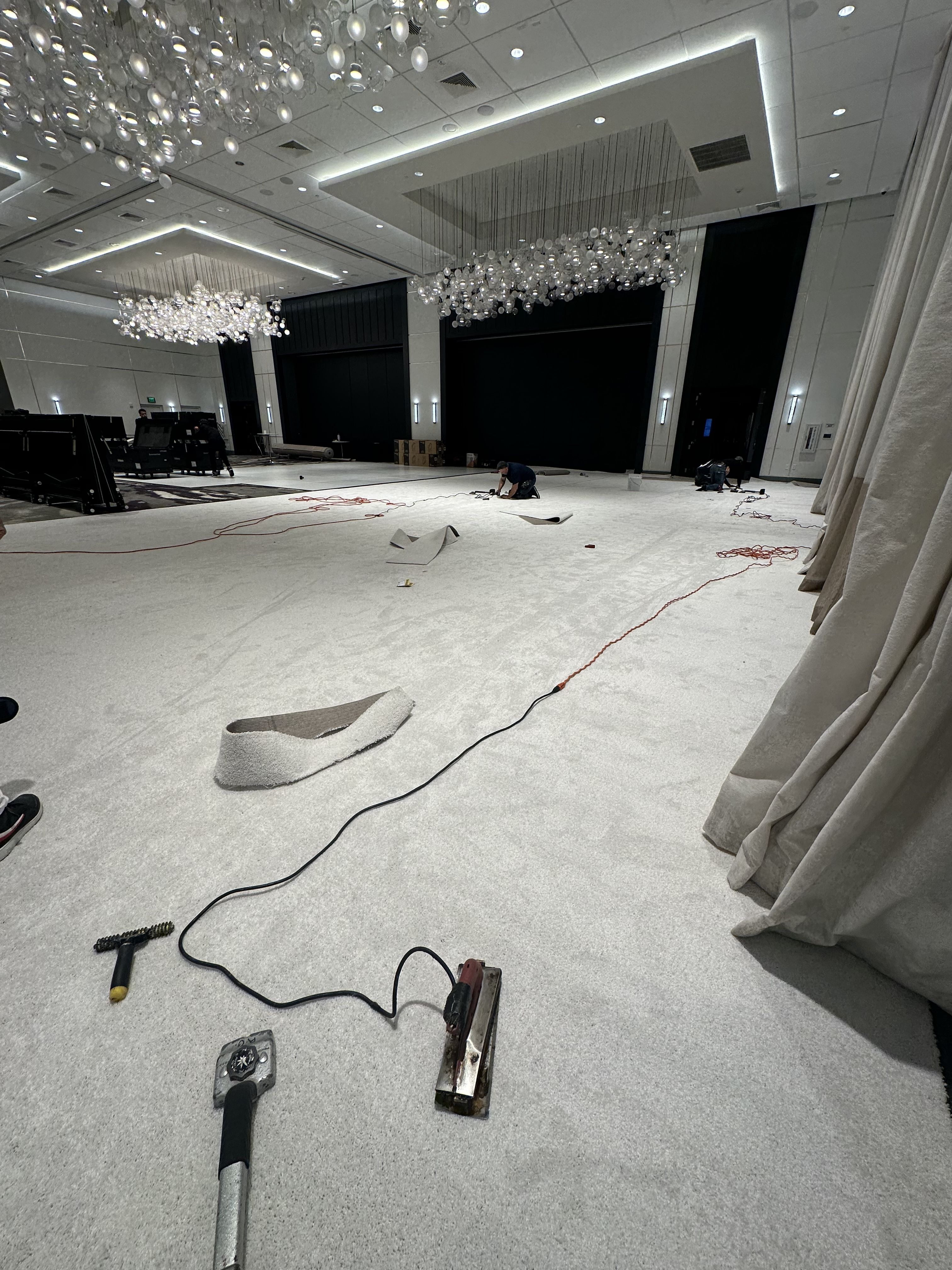 White event carpet being cut and seamed in a ballroom under chandeliers