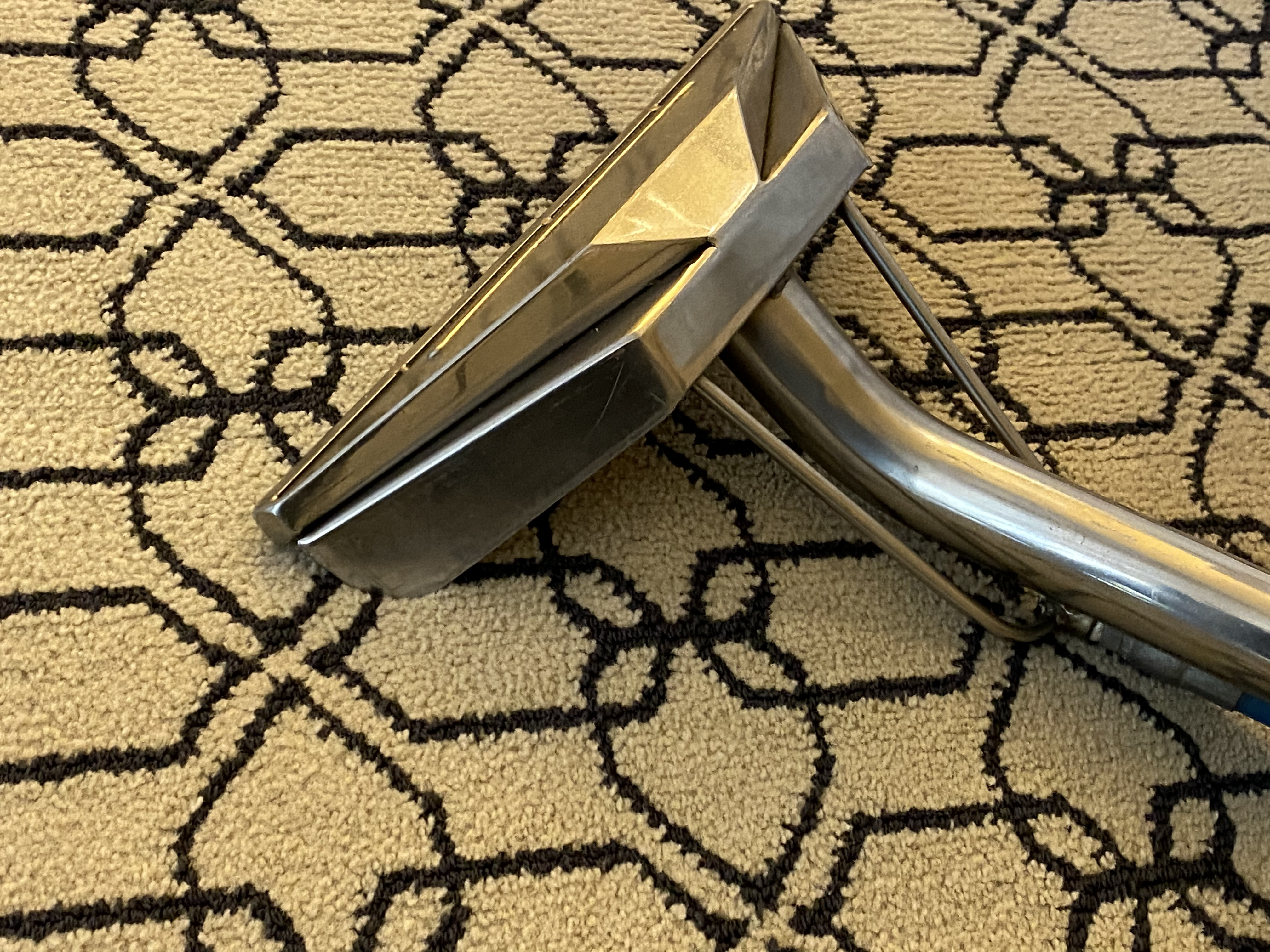 Close-up of a carpet extraction wand cleaning patterned commercial carpet