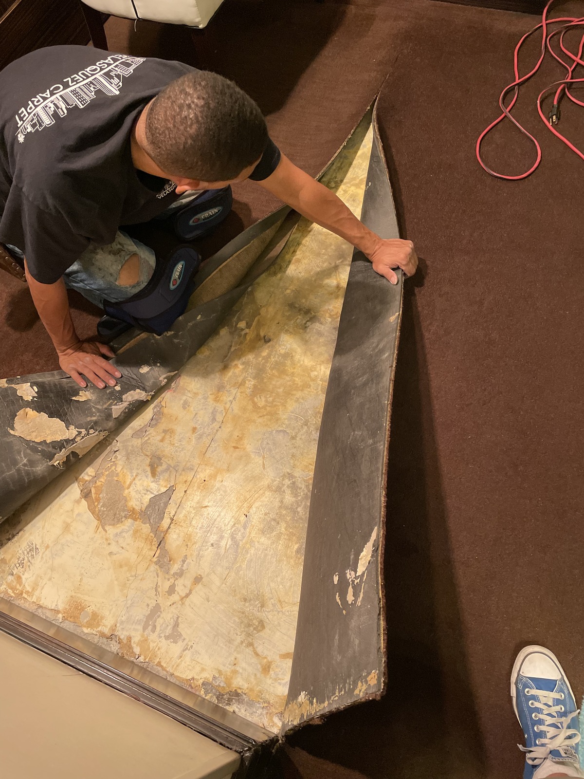 Velasquez Carpet installer lifting a worn commercial carpet section to inspect the backing before repair