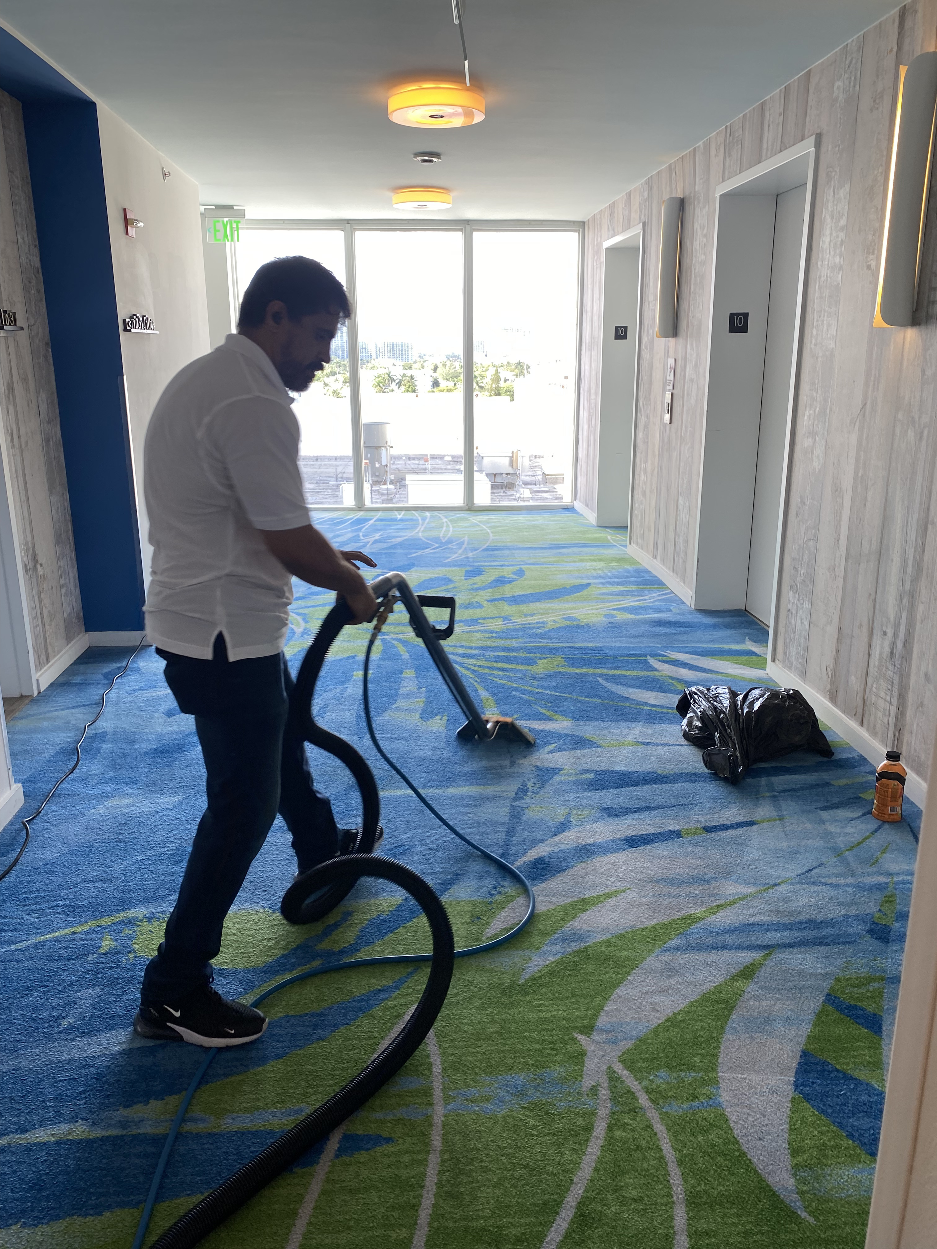 Technician cleaning patterned carpet in a hotel corridor