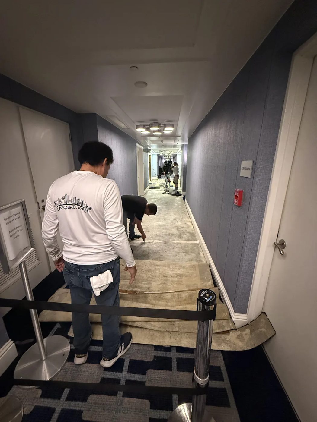 Crew removing old glued-down carpet from a hotel hallway